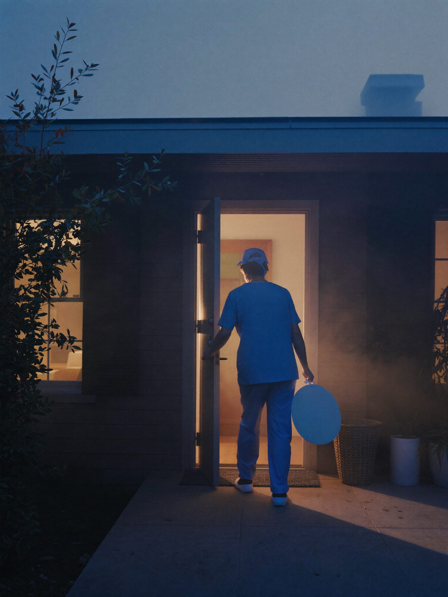 A nurse arriving home at dawn, warm porch light spilling onto the steps